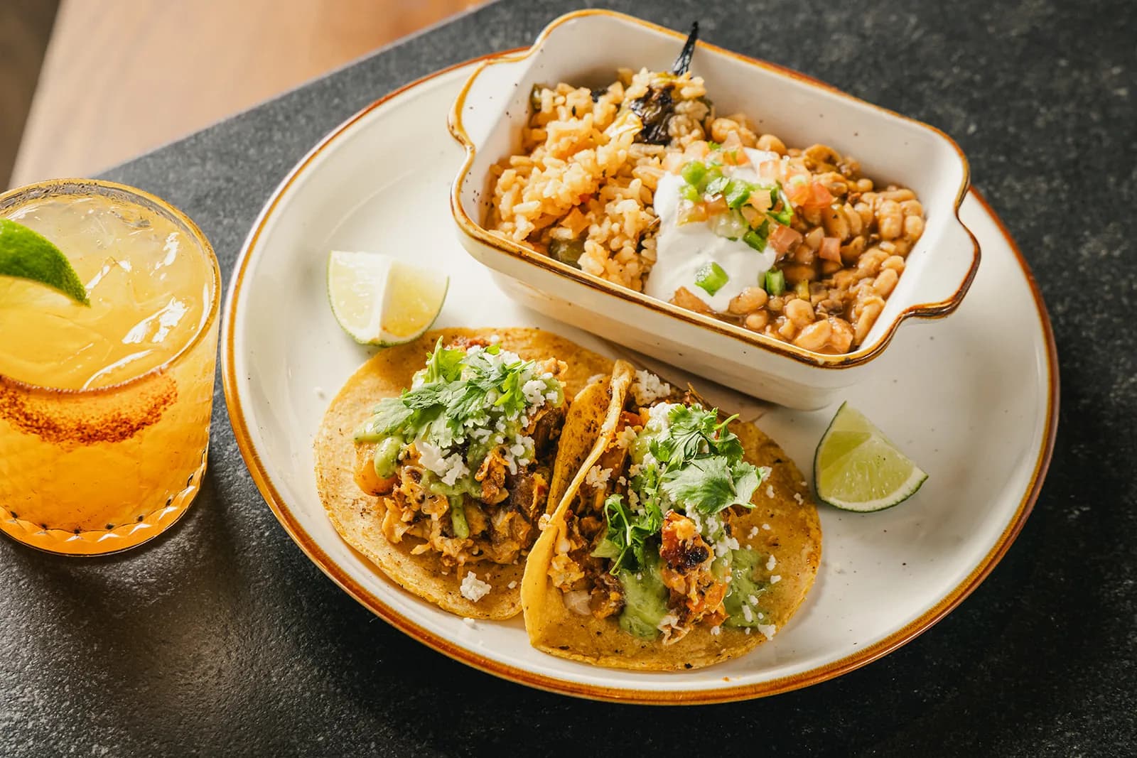 A trio of tacos on handmade tortillas with grilled esquites and a margarita